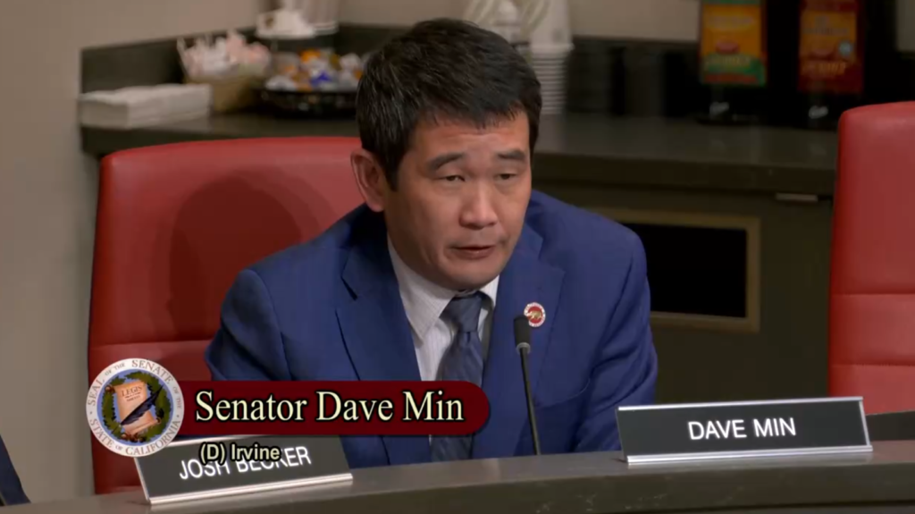 Photo of Senator Dave Min sitting behind a microphone in a business suit, speaking.